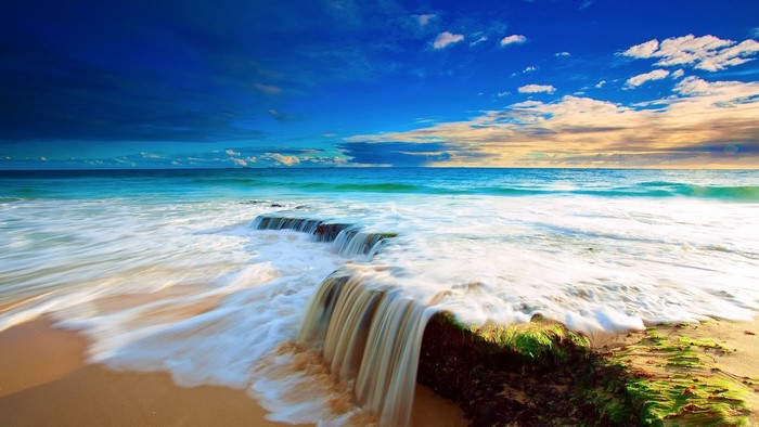 Ocean waves crashing on a sandy beach with rocks