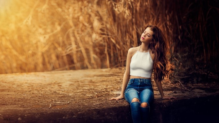Girl in white top and ripped jeans sitting outdoors