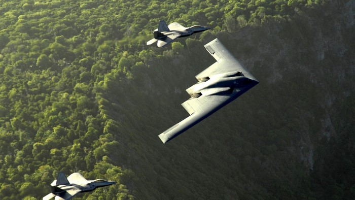 F-22 Raptors and B-2 Bomber flying over forest