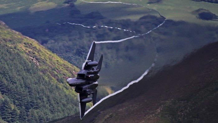 F-15 Eagle jet leaving contrails over mountains