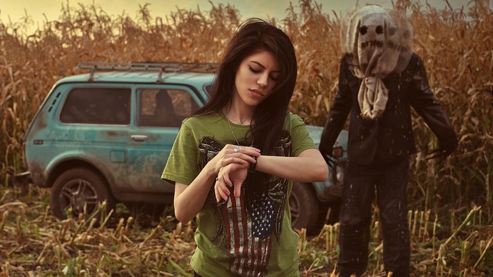 Girl checking watch with scarecrow in cornfield