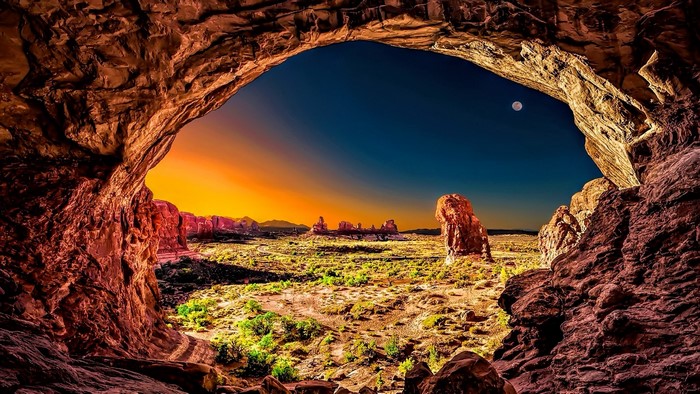 Cave entrance overlooking desert landscape at sunset with moon