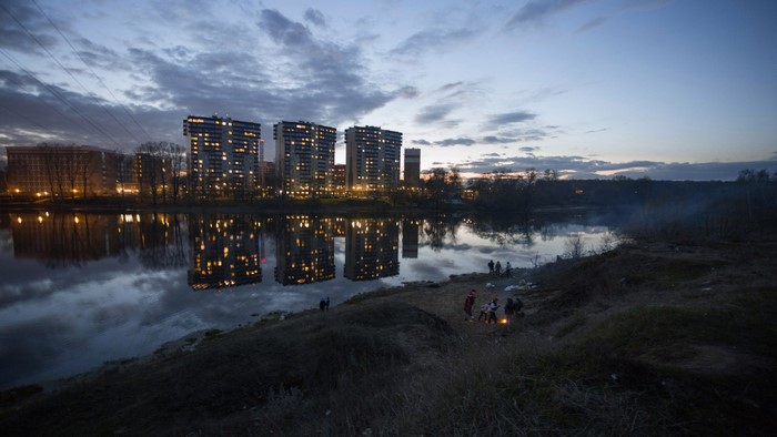 Apartment buildings reflected in a river at dusk with people by the shore