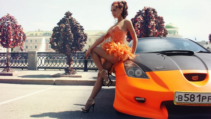 Woman in orange dress posing with orange sports car
