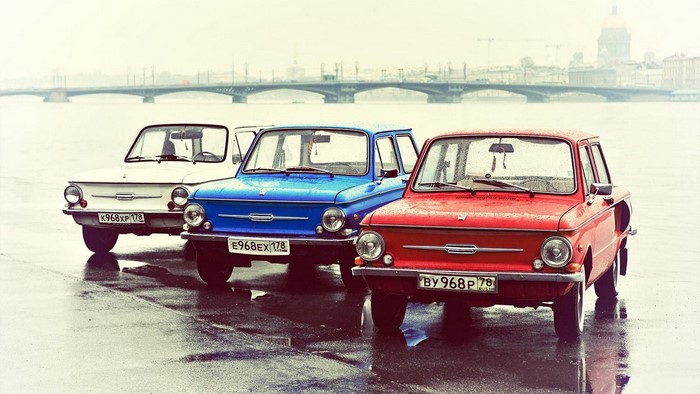 Three ZAZ cars parked by a river with a bridge in the background