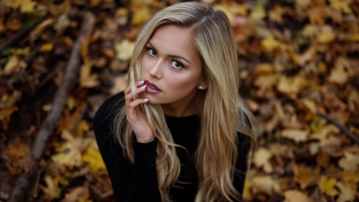 Blonde woman with makeup sitting in autumn leaves