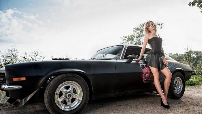 Woman in corset and skirt posing by a black car