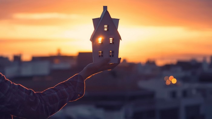 Hand holding a model house at sunset