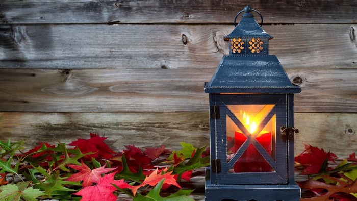 Lantern with candle and autumn leaves on wooden background