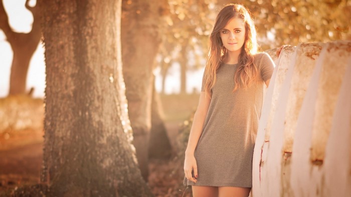 Young woman in a grey dress leaning on a wall