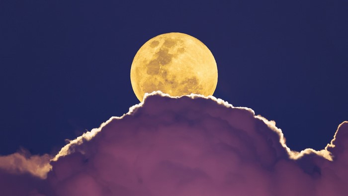 Full moon rising above purple clouds