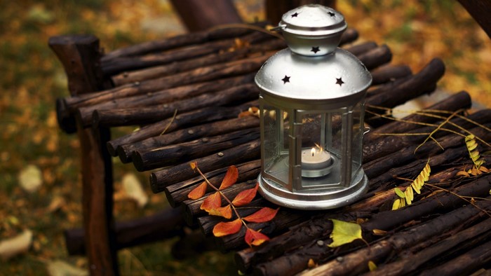 Lantern with lit candle on wooden surface in autumn