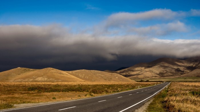 Road through hills under cloudy sky