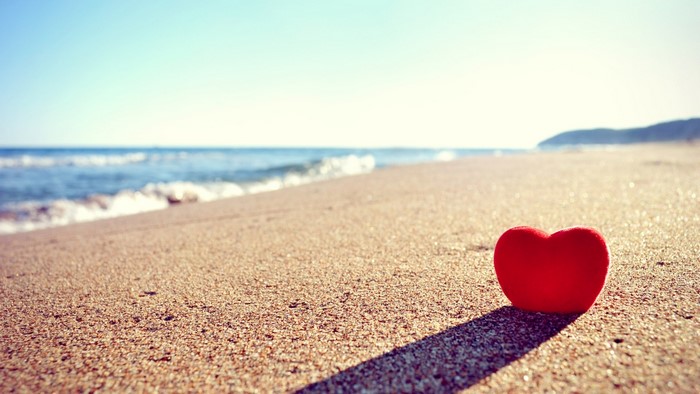 Red heart on a sandy beach with ocean waves