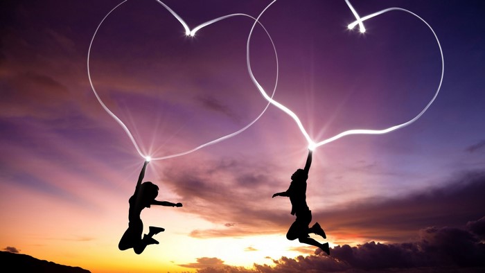 Couple drawing hearts in the sky at sunset