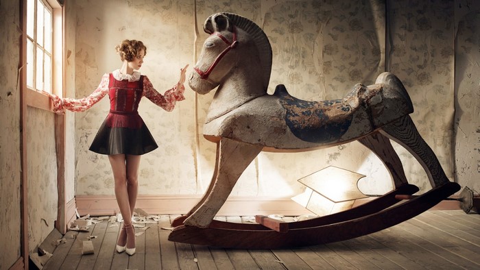 Woman with rocking horse in abandoned room
