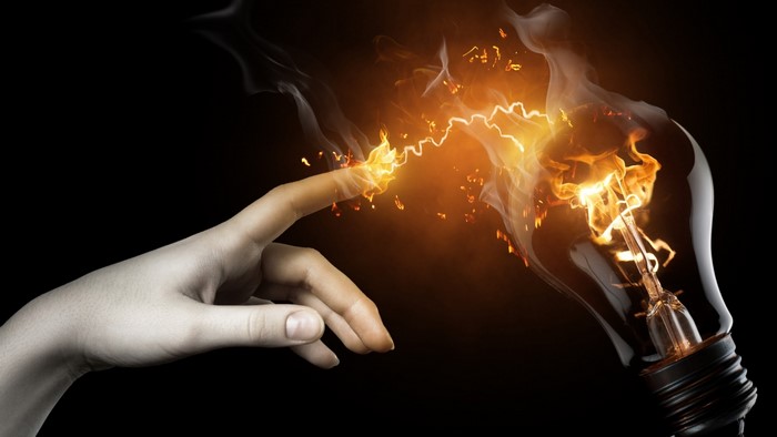 Finger touching a burning light bulb with sparks