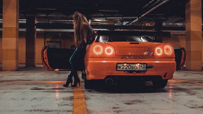 Woman leaning on a Nissan Skyline R34 GTT