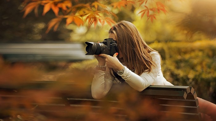 Woman with camera taking photos in autumn park
