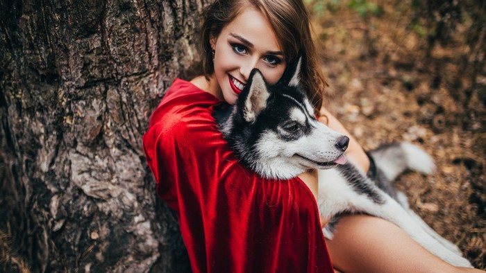 Girl in red cape with husky dog by tree