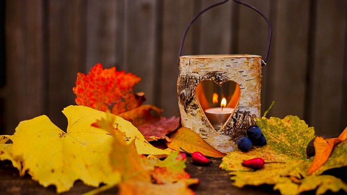 Autumn leaves and a lit candle in a wooden lantern