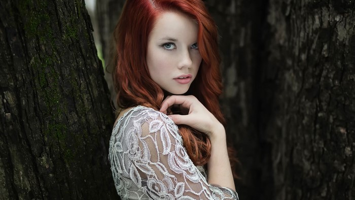 Woman with red hair in a lace dress near trees