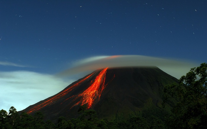 Volcano erupting lava at night under starry sky