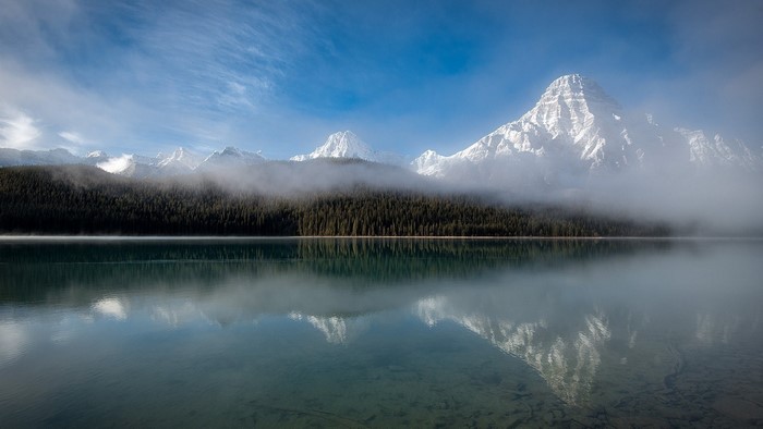 Snow-covered mountains reflected in a misty lake