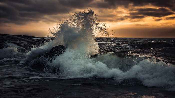 Wave crashing on rocks at sunset