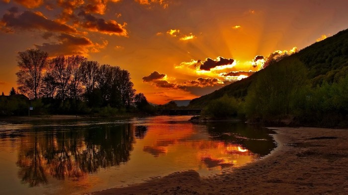 Sunset over a river with trees and mountains