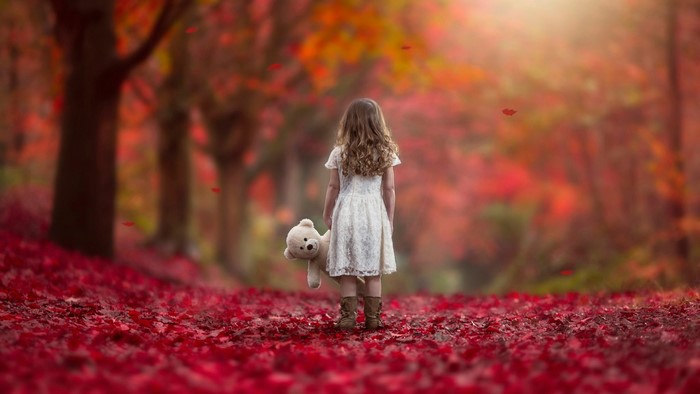 Girl with teddy bear in autumn forest
