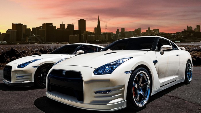 Two white Nissan GT-R cars in front of a city skyline
