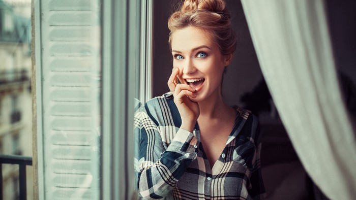Cheerful girl in plaid shirt by window