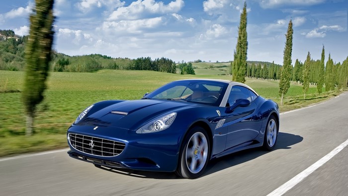 Blue Ferrari California driving on a scenic road