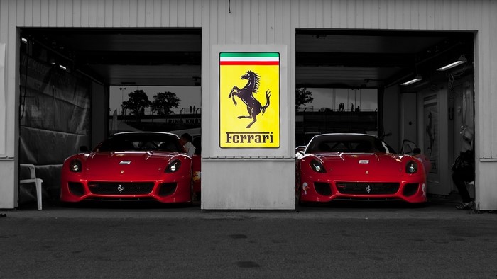 Two red Ferraris in a garage with Ferrari logo
