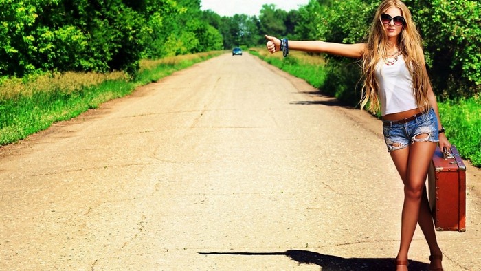 Woman hitchhiking with suitcase on rural road