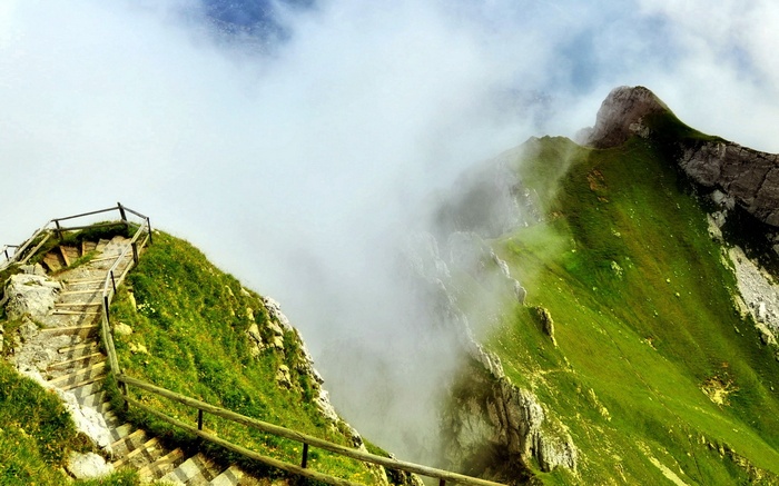 Wooden stairs on a grassy mountain with clouds