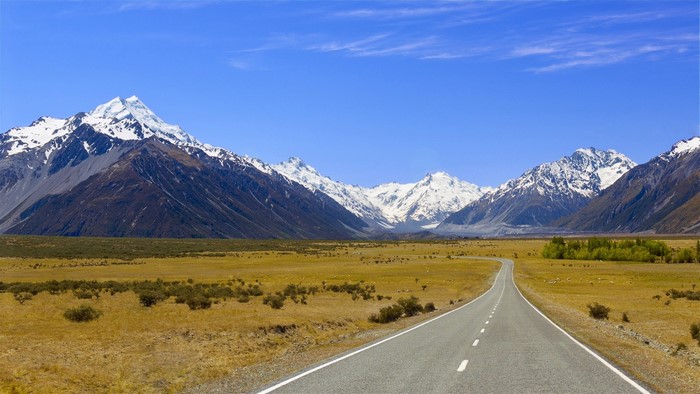 Road leading to snow-capped mountains under blue sky