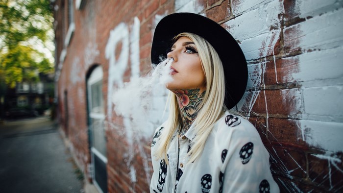 Blonde woman with neck tattoos exhales smoke