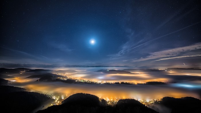 Night sky over a foggy valley with city lights