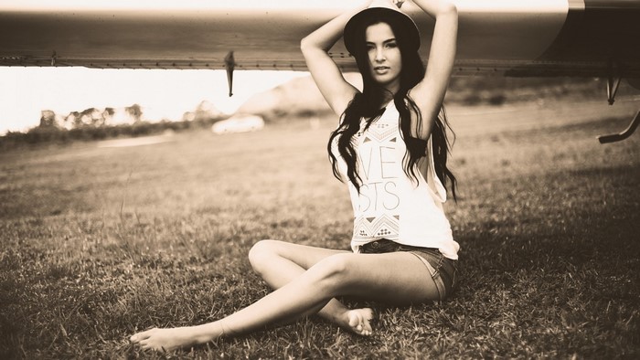 Girl in hat and shorts sitting by airplane