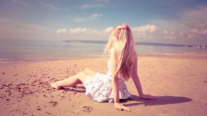 Blonde girl sitting on a beach by the sea