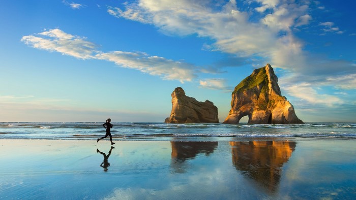 Person jogging on a beach with rock formations