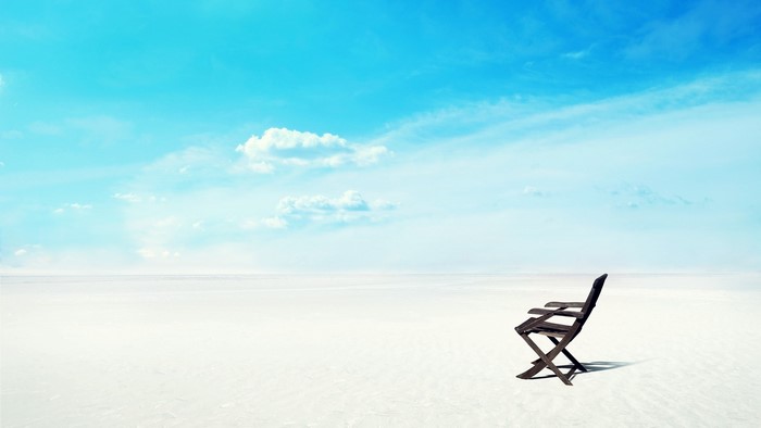 Empty beach with a single chair under a blue sky