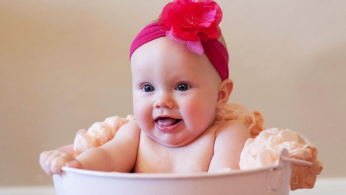 Baby girl with pink headband in a tub