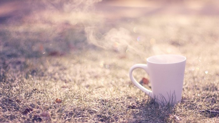 Close up of a steaming coffee mug on grass