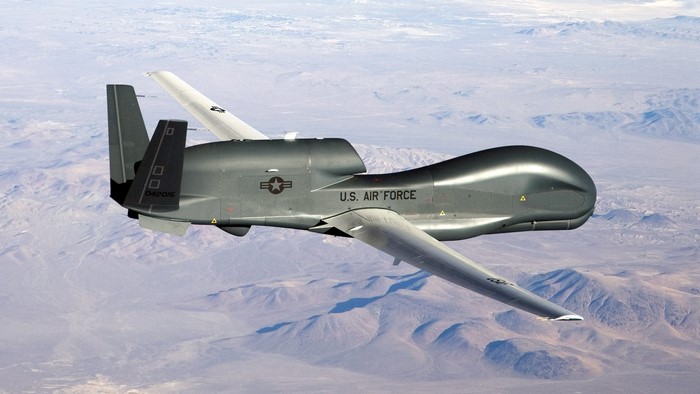 RQ-4 Global Hawk drone in flight over desert mountains