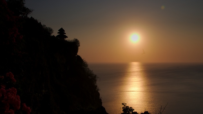 Sunset over the ocean with a cliffside temple