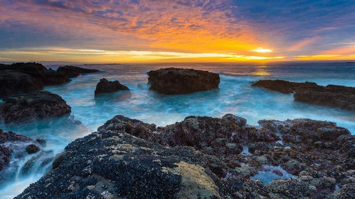 Sunset over rocky sea coast with crashing waves