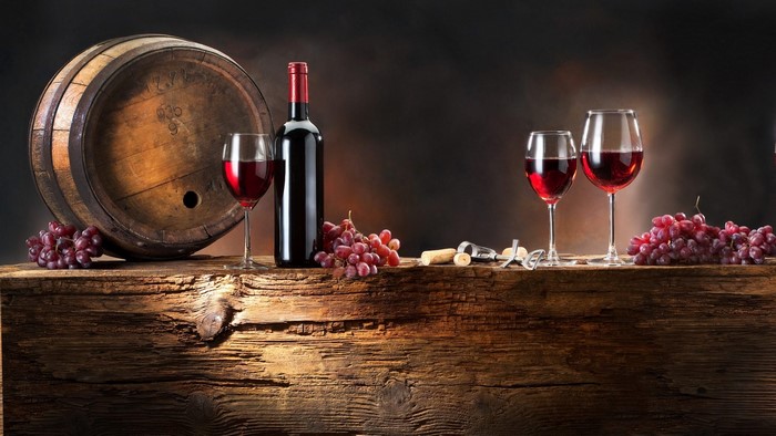 Wine barrel, bottle, glasses, and grapes on wooden table